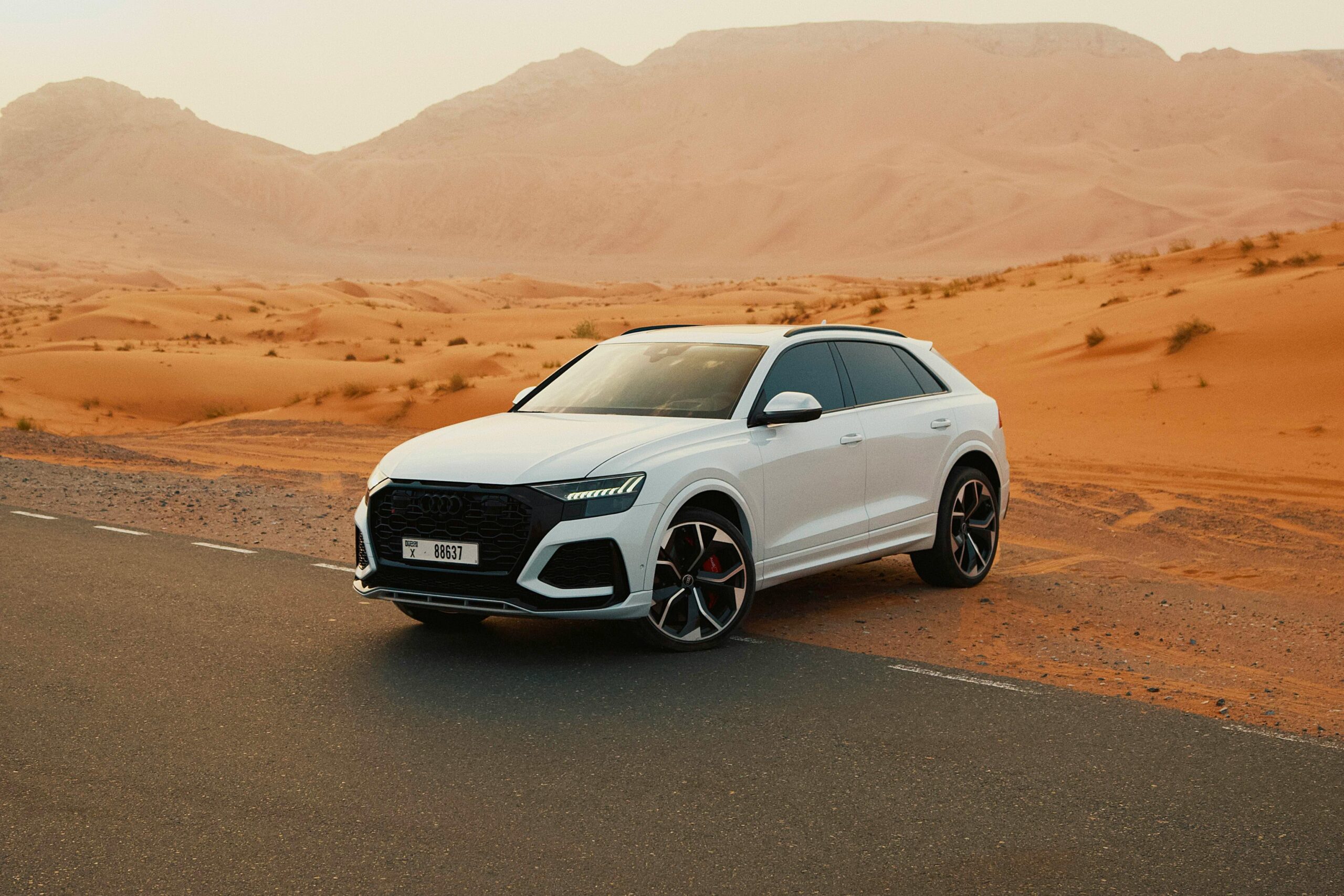 White luxury SUV parked on desert road during sunset, showcasing elegance amid the dunes.